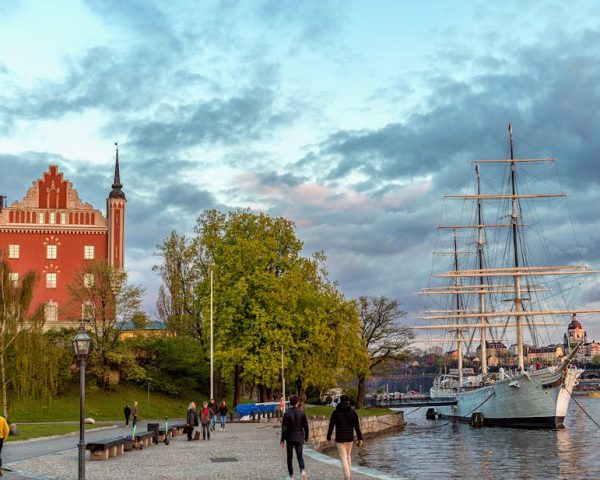 A beautiful waterfront scene in Stockholm with a historic ship and the iconic red building under a cloudy dusk sky.